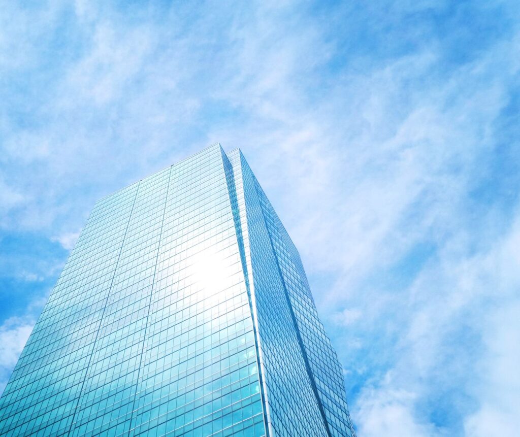 Low-angle view of a modern skyscraper with reflective glass walls against a clear blue sky.