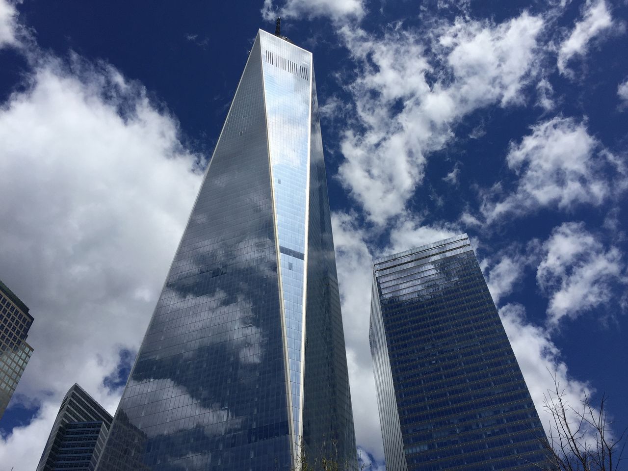 A breathtaking low-angle perspective of modern skyscrapers with reflections and clouds in a clear blue sky.