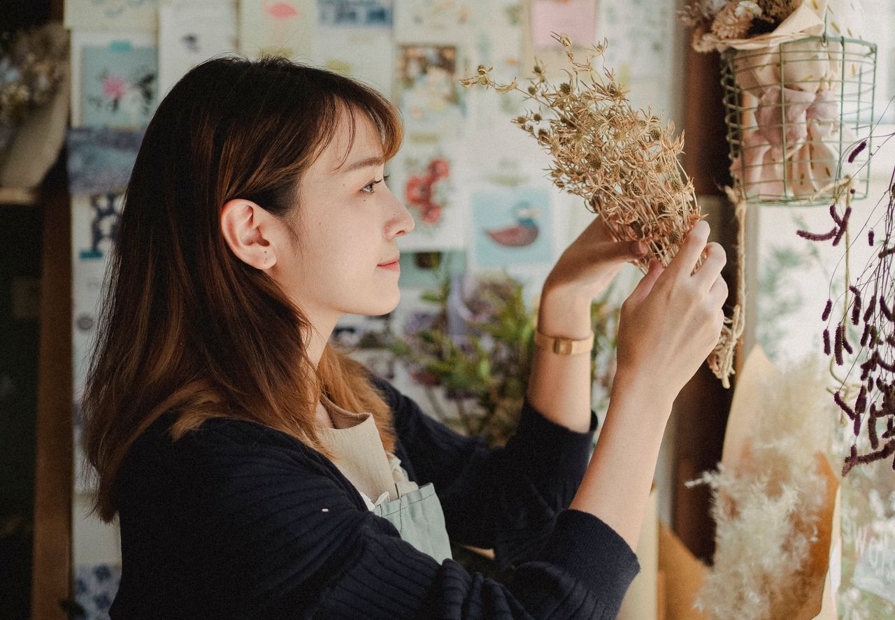 Side view of young woman in apron standing in floral shop and holding dry flowers